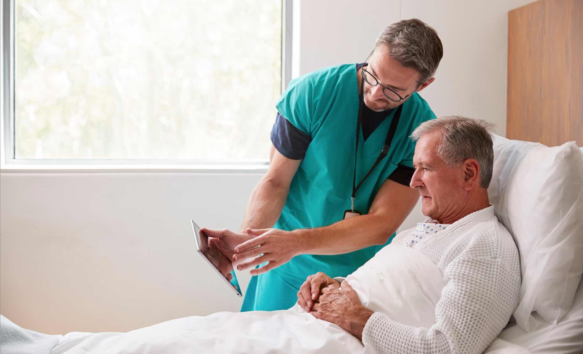 Vårdbiträde visar information på ipad för patient.