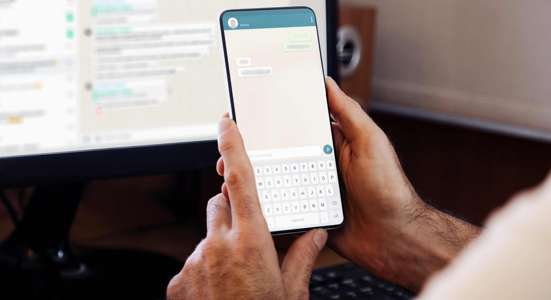 Hand med mobil framför en dator.